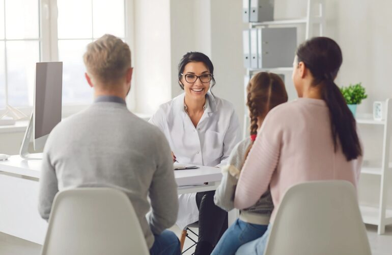 Pessoa acompanhado por um familiar durante uma consulta auditiva, enquanto um fonoaudiólogo explica sobre aparelhos auditivos. A imagem representa a importância do apoio familiar na adaptação à perda auditiva.